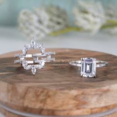 two engagement rings sitting on top of a wooden box with flowers in the back ground