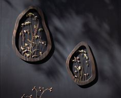 two wooden wall hangings with dried flowers in them on a black wall next to each other