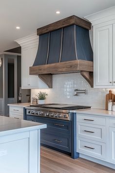 Modern kitchen with white cabinets, blue island, and large wood-accented kitchen hood over the stove. Modern Kitchen Range, Country Chic Kitchen, Wooden Range Hood, Lake Kitchen, Chimney Range Hood