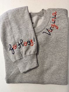 two sweatshirts with writing on them sitting next to each other, one is grey and the other is red