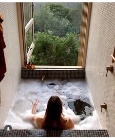 a woman is sitting in the bathtub with her hands up and looking out the window