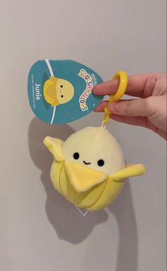 a hand holding a yellow stuffed animal with a tag on it's ear and another toy in the background