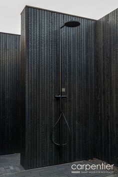 the shower head is mounted on the wall next to the black tiled floor and walls