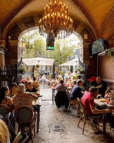 people are sitting at tables in an outdoor dining area with chandelier above them