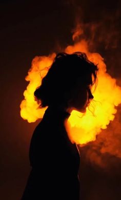 a woman standing in front of a fireball with her head turned to the side