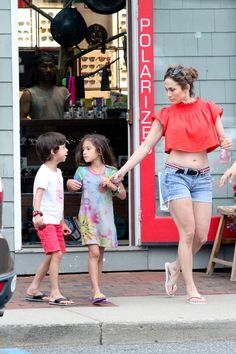 a woman walking with two children in front of a storefront and the child is holding her hand