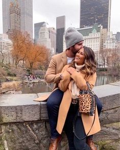 a man and woman sitting on top of a stone wall in front of a cityscape