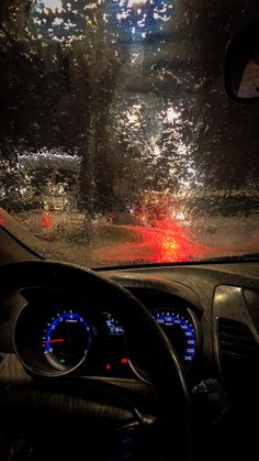 the dashboard of a car is covered in rain and red light at night, as seen from inside