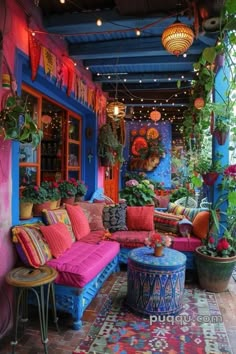 an outdoor patio with colorful furniture and potted plants on the wall, lights strung from above