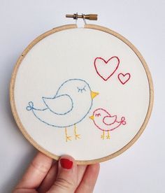 a hand is holding a small embroidery hoop with two birds on it and hearts in the background