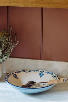 a blue and white bowl sitting on top of a counter next to a vase filled with flowers