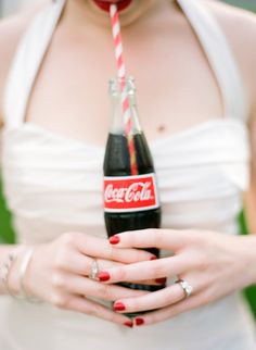 a woman in white dress holding a coca cola bottle with red and white striped straw