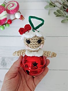 a hand holding a red ornament with a small doll on top of it