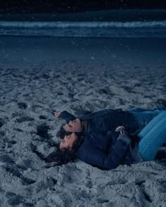 a man and woman laying on the beach in the sand at night with their eyes closed