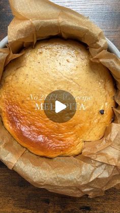 a loaf of bread sitting in a bowl on top of a wooden table next to a paper bag