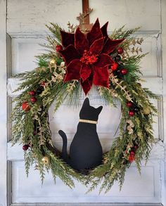 a black cat sitting in front of a wreath with poinsettis on it