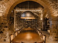 a wooden table and chairs in a room with stone walls, arched doorways and a metal light fixture hanging from the ceiling