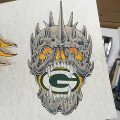 a drawing of a green bay packers skull with spikes on it's head and an image of a football helmet in the background