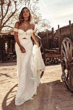 a beautiful woman in a white dress standing next to a wagon and holding a bag