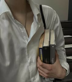 a person holding two books in their hands while wearing a white shirt and black cross - body bag