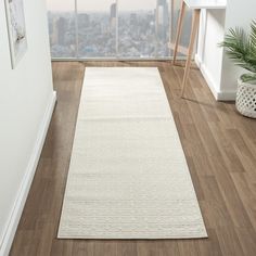 a large white rug in the corner of a room next to a window with city view