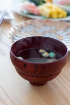 a wooden bowl filled with liquid on top of a table next to plates and utensils