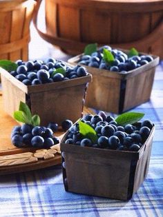 three wooden containers filled with blueberries sitting on top of a checkered table cloth