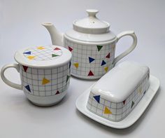 three pieces of pottery are sitting on a table top, one has a teapot and the other has a cup with a lid