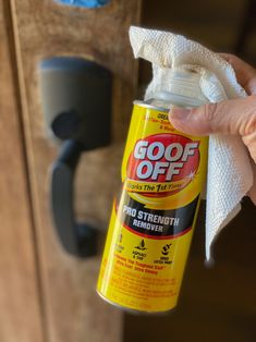 a hand holding a bottle of goof off deodorant next to a cabinet