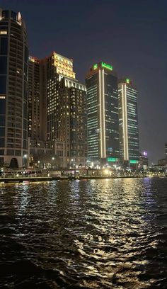 the city skyline is lit up at night by the water's edge, with skyscrapers in the background