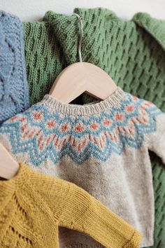 sweaters and mittens hanging on a rack with wooden clothes hangers in front of them