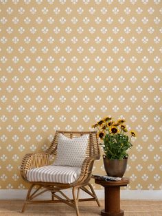 a wicker chair next to a potted sunflower on a table in front of a wall