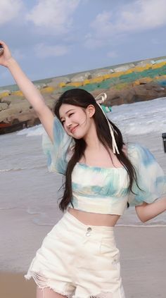 a woman standing on top of a beach next to the ocean holding up a can