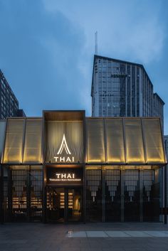 the entrance to a thai restaurant with tall buildings in the background at dusk, lit up by neon lights