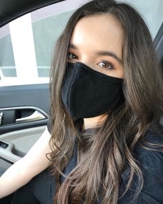 a woman wearing a black face mask sitting in a car with her hand on the steering wheel