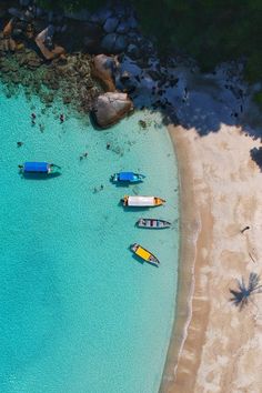 several small boats floating on top of a blue body of water next to a sandy beach