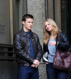 a man and woman standing next to each other in front of a building holding hands