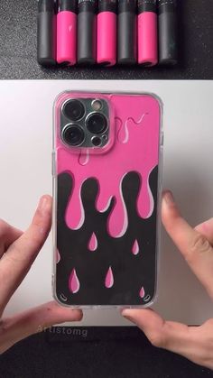 someone is holding up their phone case with pink and black liquid drops on the back