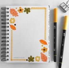 an open notebook with flowers and leaves on it next to a marker, pen and clipboard