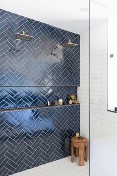 a bathroom with blue tiled walls and white tiles on the shower wall, along with a wooden stool