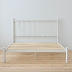 a white bed frame sitting on top of a hard wood floor next to a wall