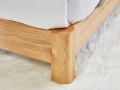 a wooden bed frame with white pillows on top of it and a fluffy rug in the background