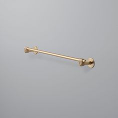 an antique brass towel bar on a gray wall with two handles and one end pointing upward