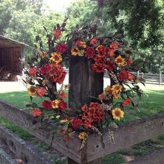 a wreath made out of flowers on top of a wooden fence in front of a barn