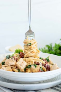 pasta with chicken and spinach in a white bowl on a striped place mat, next to a fork