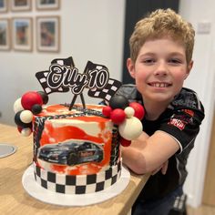 a young boy sitting at a table with a cake in front of him that has cars on it