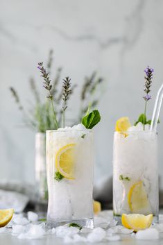 two glasses filled with lemonade and lavender sprigs on top of ice cubes