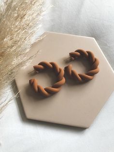 a pair of brown earrings sitting on top of a white table next to dried grass