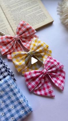 four different colored bows are sitting on a table next to an open book and yarn