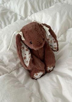 a brown stuffed animal sitting on top of a white bed sheet covered in sheets and pillows